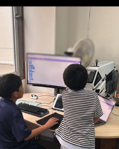 小学生が友だちと一緒にプログラミング作品を見ている様子