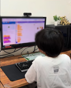 小学生が後ろ姿でパソコン画面に向かい体験学習をしている様子