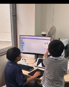 小学生二人が並んでパソコンに向かいプログラミング学習をしている様子