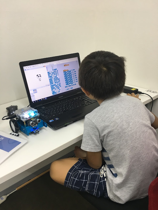 Scratchのブロックを使ってプログラミングを学ぶ小学生の後ろ姿