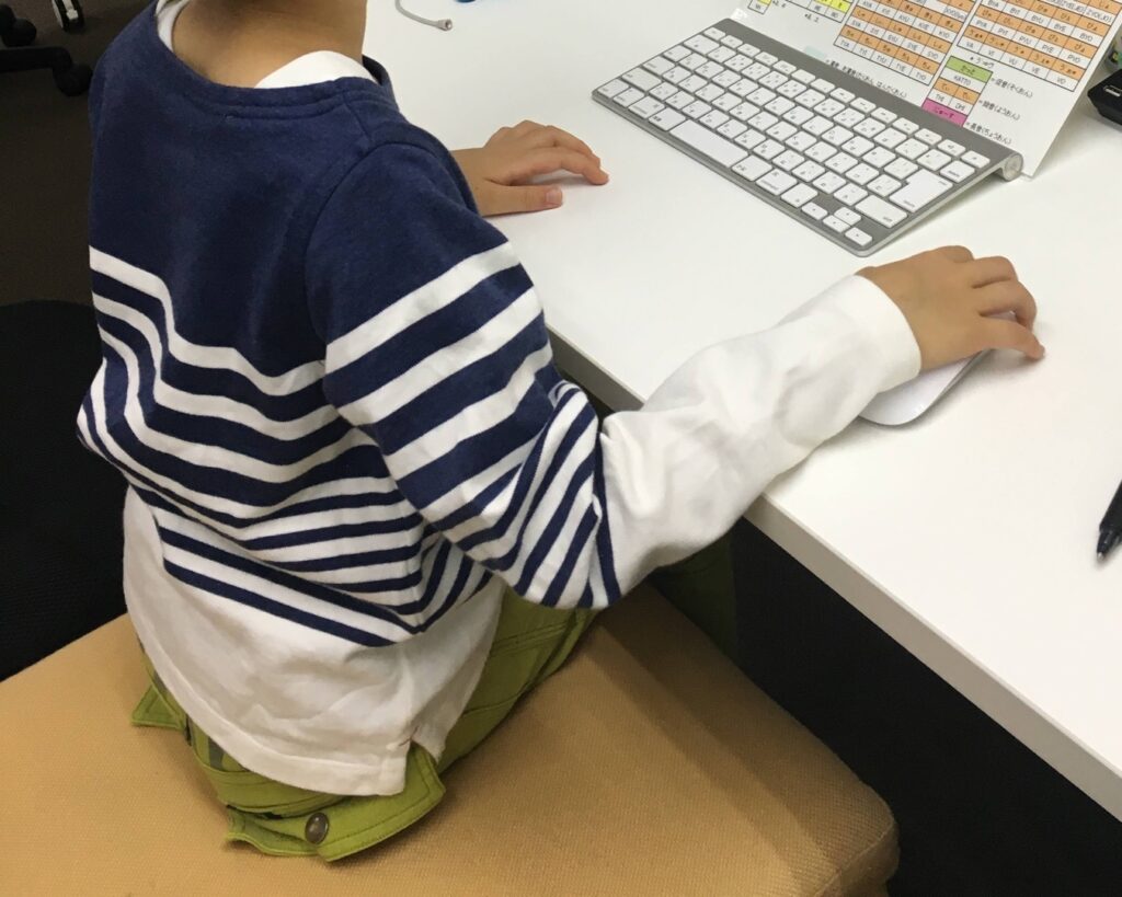 背中を向けてScratchの画面を見ながら、キーボードとマウスで操作する子どもの手元