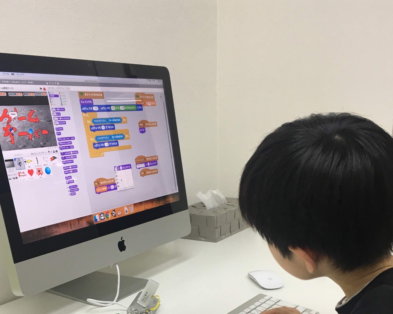 子どもが後ろ姿でパソコン画面のScratch作品を操作している学習風景